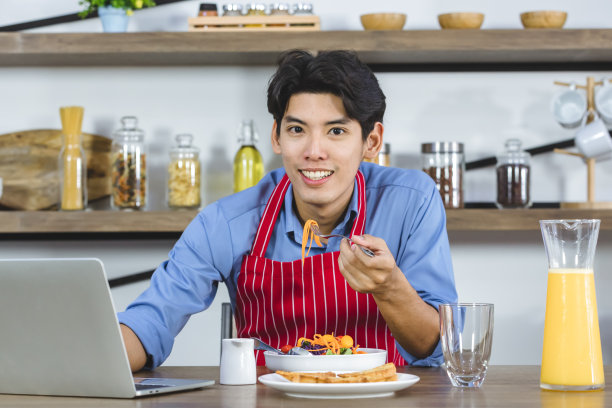 亚洲男子吃沙拉时用笔记本。图片下载