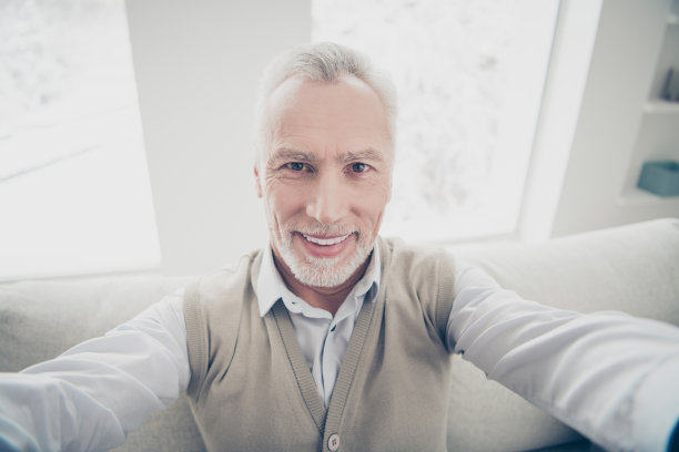 近距离的照片惊人的男子，他，他，他的老人，使自拍友好的，积极的，现代的，白色的，完美的，理想的牙齿，穿着白色的衬衫，马甲，裤子，舒适的沙发，公寓，客厅，室内图片下载