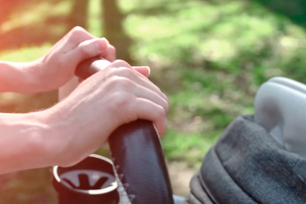 母亲的手推着婴儿车和熟睡的婴儿在夏天的绿色公园。模糊的，没有焦点的照片背景图片下载