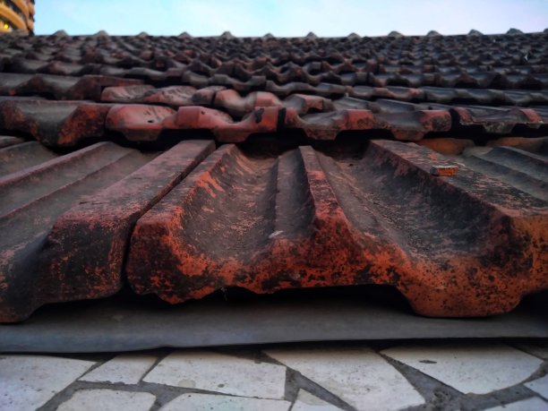 旧的和肮脏的倾斜的暗棕色粘土瓦屋顶和山脊近距离图像的农村地区的房子。图片下载