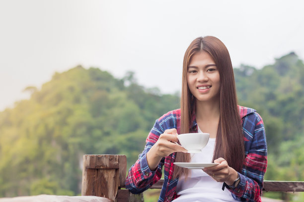 美丽的女人捧着一杯咖啡，背景是美丽的山景。图片下载
