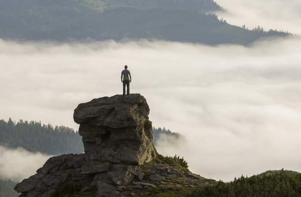 运动员攀岩游客的剪影在高岩石形成的山谷充满白色的蓬松的云和雾，覆盖常绿的森林山坡在晴朗的天空背景下。图片下载