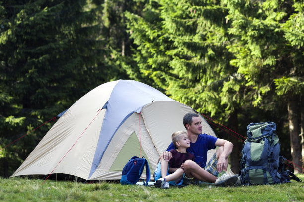 假日野营。父亲和他的儿子在森林徒步旅行和户外活动后在帐篷附近休息。幸福的家庭关系和健康的生活方式。图片下载