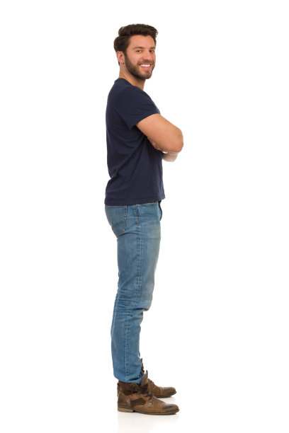 穿着牛仔裤和蓝色t恤的年轻人双臂交叉站着。侧视图。图片下载