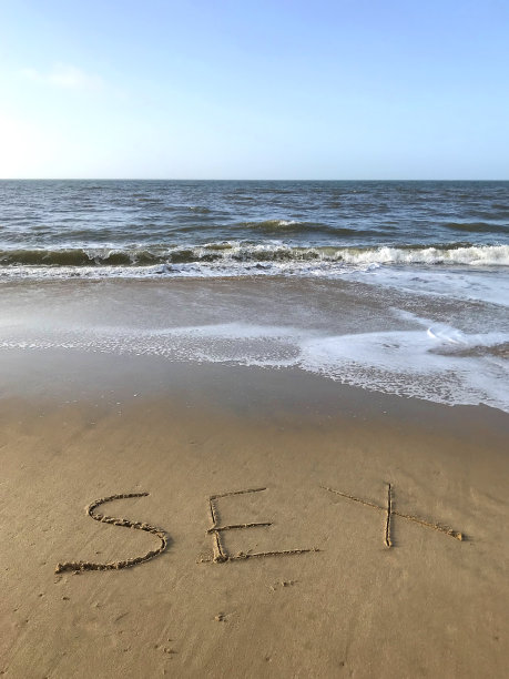 这是在阳光明媚的海滩上写的照片，用木棍在沙滩上写下性的词语，海浪，概念社交媒体上的照片，在柔软的金色沙滩上写的字母，多塞特，英国海边的海岸线图片下载