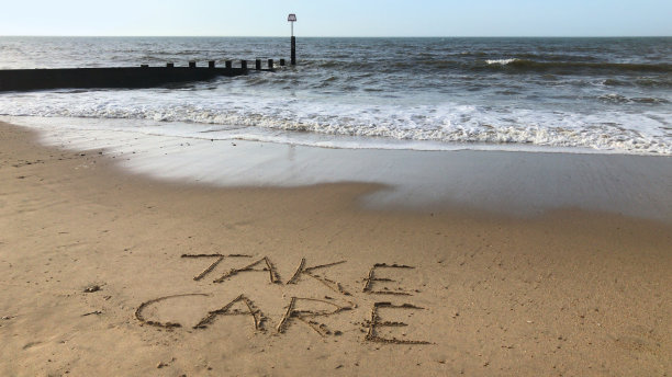 在阳光明媚的海滩上用棍子写的“小心”字，海浪，概念社交媒体照片在伯恩茅斯海滩柔软的金色沙滩上手写字母，多塞特，英国海边的海岸线图片下载