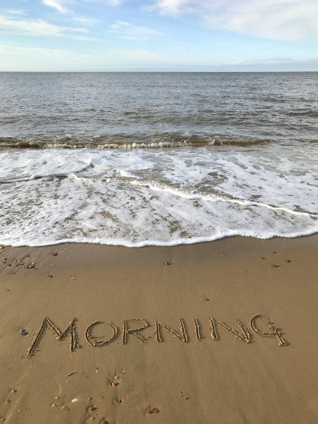 图片写在阳光明媚的海滩上，早上的单词写在沙子上，用棍子，海浪，概念社交媒体的照片手写字母在柔软的金色沙滩上，多塞特，英国海边的海岸线图片下载