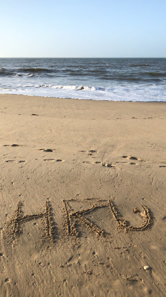 在阳光明媚的海滩上用HRU书写的图像/你如何在沙子上用棍写的话，由海浪，概念社交媒体照片在柔软的金色沙滩上书写字母，多塞特，英国海边海岸线的景色图片下载