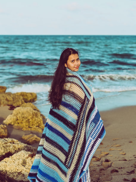 舒适的海滩，年轻女子裹着毯子躺在沙滩上图片下载