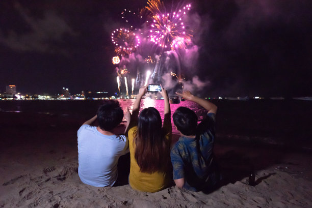 一群朋友享受和拿着智能手机拍摄多彩的烟花显示在夜空背景的海滩图片下载