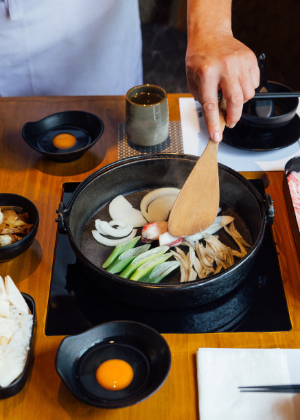 厨师先将洋葱、葱和蘑菇放入素喜烧火锅中炒熟，再加入烧制的烧酒汤，煮出和牛和黑田鸡肉。图片下载