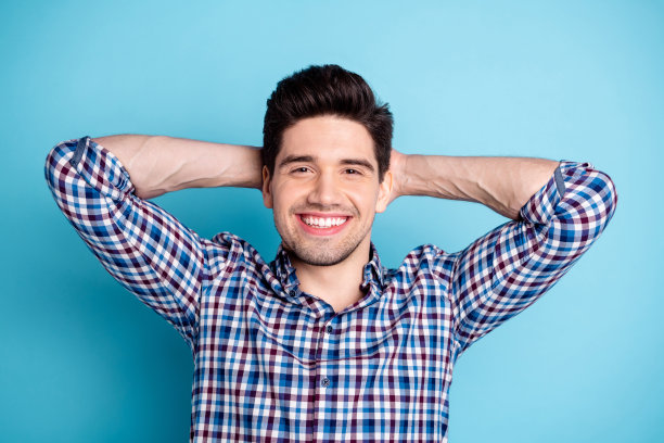 近距离的照片惊人的有趣，他他，他的大男子主义的白牙齿，手，手臂后面的头，健康的，清新的样子，休息日，假日，穿休闲的格子衬衫孤立的亮蓝色背景图片下载