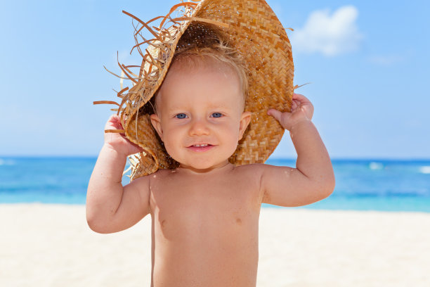 在阳光明媚的热带海滩上，戴着草帽的快乐男婴图片下载