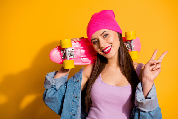 近距离的照片美丽的她她的女士好看的手手臂滑板危险的运动v标志牙齿光滑的嘴唇穿着休闲牛仔裤牛仔夹克鞋粉色的帽子孤立的黄色生动的背景图片下载