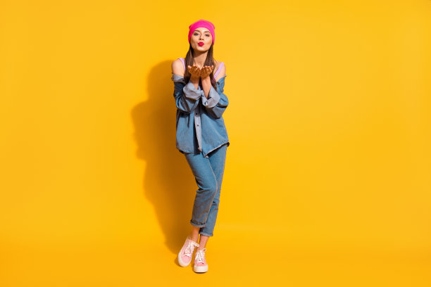 全身的身体尺寸照片美丽有趣的她，她的少女长头发，手，手臂张开的手掌，送空气吻，口红，穿着休闲的牛仔裤，牛仔夹克，鞋子，粉红色的帽子孤立的黄色明亮的背景图片下载