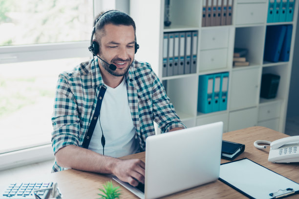 特写照片英俊的他他他的家伙耳机说话麦克风客户回答问题帮助帮助购买买家呼叫中心工作笔记本桌子坐办公椅穿格子衬衫图片下载