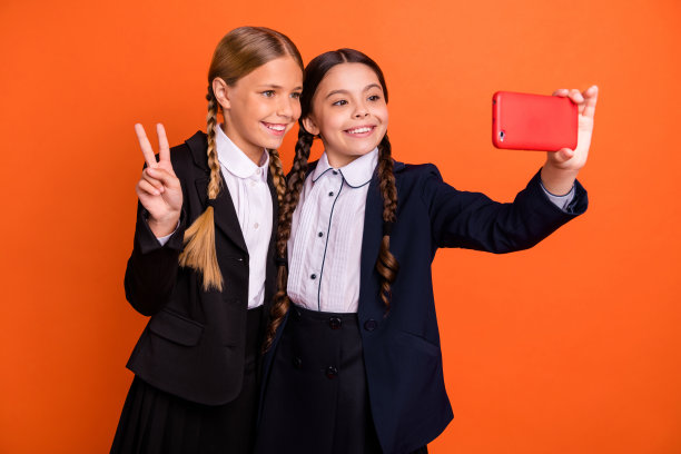 近距离的照片美丽的她她的小妹妹女士手手臂v标志符号电话做自拍说嗨instagram穿正装衬衫夹克学校形式包孤立明亮的橙色背景图片下载