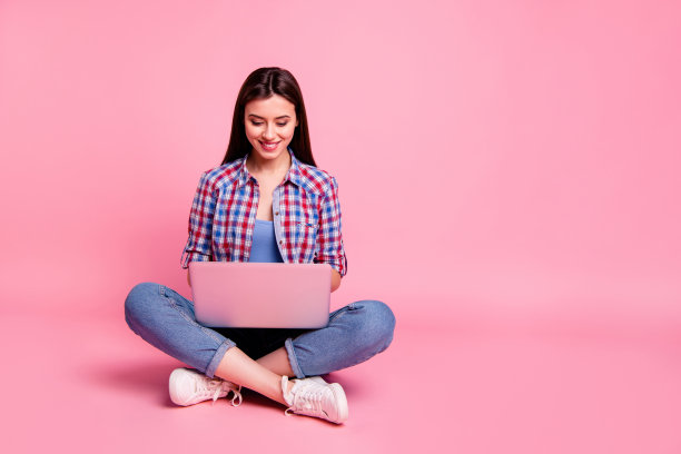 全身的身体尺寸照片美丽的她她的夫人坐地板跷腿笔记本膝盖聊天外国朋友短信兴奋穿休闲格子衬衫牛仔裤牛仔孤立的粉色背景图片下载