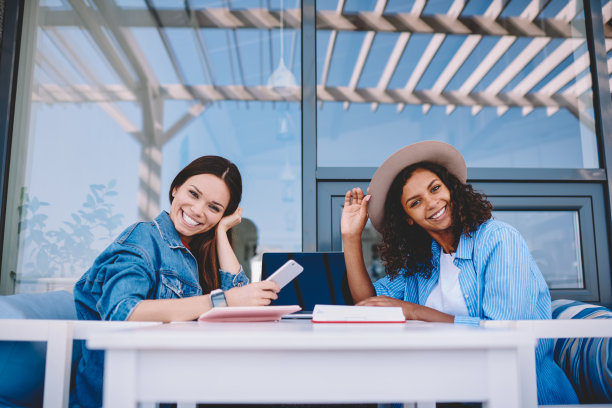 照片上的女性朋友们穿着时髦的衣服，一起在户外咖啡馆享受时光，兴奋的千禧一代女性在使用科技和良好的互联网连接时看着相机图片下载