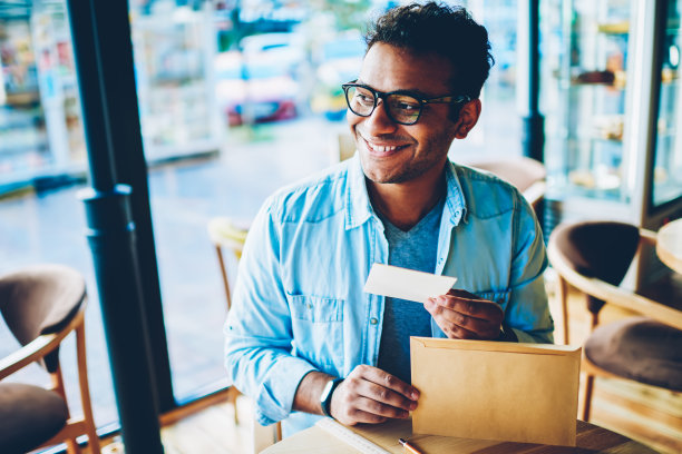 英俊微笑的印度男性企业家的特写图片从浅棕色的包裹和兴奋的内容小信件。成熟的好看的快乐的男人在凉爽的眼镜坐在咖啡馆图片下载