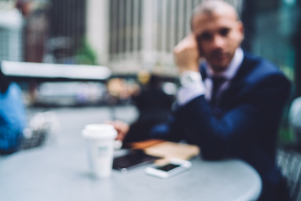 一张模糊的照片，帅气的商人穿着优雅的正装看着相机，坐在街头的咖啡馆里，喝着咖啡和现代科技，花时间做会计报告图片下载