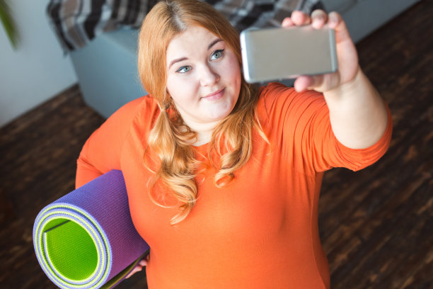 胖乎乎的女人在家里站着自拍与垫子微笑图片下载