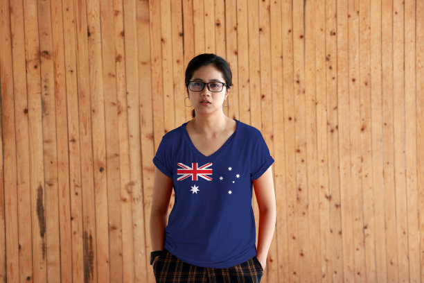 一个女人穿着澳大利亚国旗颜色的衬衫，双手插在裤子口袋里，站在木墙的背景上。图片下载