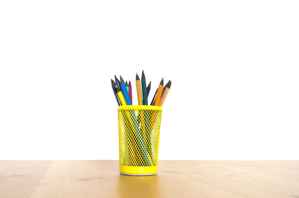 白色背景的木桌上，黄色玻璃杯里的彩色铅笔图片下载