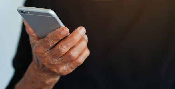 近距离退休的老年妇女手持智能手机观看娱乐媒体上的网站，在家中客厅老年人的良好生活方式的概念图片下载