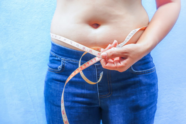 正面图，胖女人正在测量她的腰围。图片下载