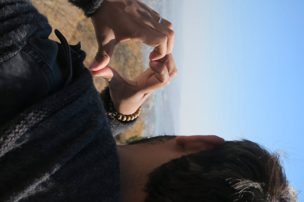 男人与爱的心手形成剪影形状对太阳蓝色的天空，心手形状形成的手指在男人的头上作为概念墙纸照片的夫妇的爱情，浪漫，婚礼主题与情人节心形象征的手/手指图片下载