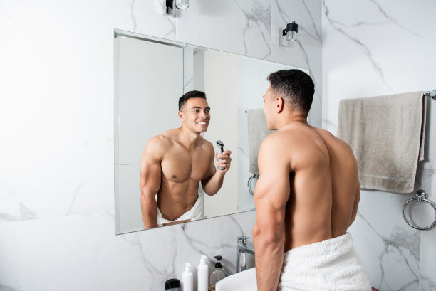 快乐的裸男在浴室里用电动剃须刀图片下载