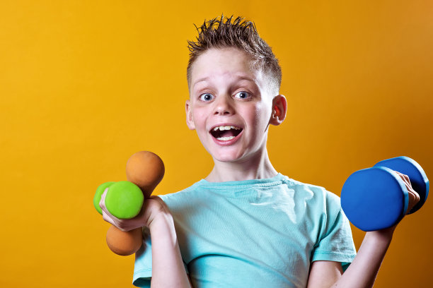 一个穿着亮t恤黄色背景上有哑铃的男孩图片下载