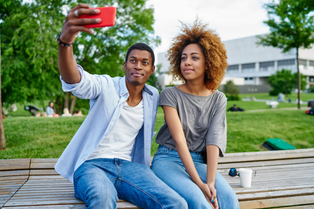 非裔美国朋友穿着休闲装，用现代智能手机的前置摄像头拍摄照片，在社交网络上发表。积极的情侣在城市设置的蜂窝自拍图片下载
