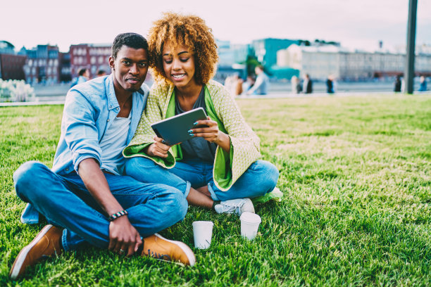 浪漫的黑皮肤情侣利用高速网络在户外社交网络上写博客，情侣们在公园约会，享受天气，通过便携式电脑上传常见的照片图片下载