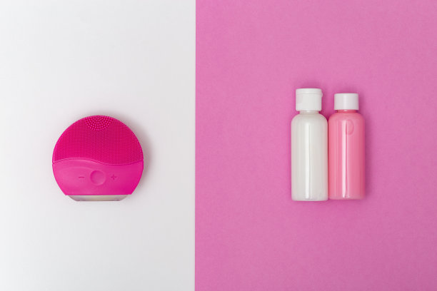 红色电动洗面刷和小瓶清洁剂，粉红色和白色的纸背景。面部清洁。美容博客的概念。平的。前视图。图片下载
