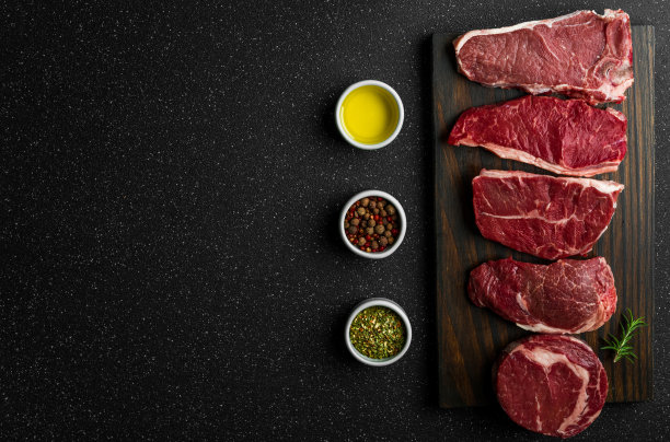 选择生牛肉肉排，以黑石为背景。纽约striploin牛排，顶级刀片，肋眼，和其他切肉。图片下载