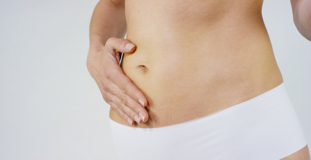 年轻的女孩涂抹奶油她美丽，完美的身体(腰部)，在一个白色的背景。图片下载