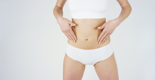 年轻的女孩涂抹奶油她美丽，完美的身体(腰部)，在一个白色的背景。图片下载