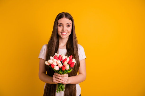近距离的照片美丽，惊人的她，她夫人，很长的头发，手，新鲜的花，白色，红色的郁金香，惊喜的节日纪念日聚会妻子，穿着休闲柔和的t恤孤立明亮的黄色背景图片下载