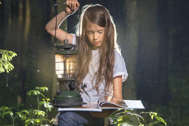 在黑暗的森林里拿着一盏灯看书。图片下载