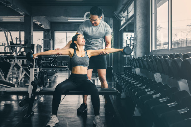 男教练在健身房用哑铃训练女性举重图片下载