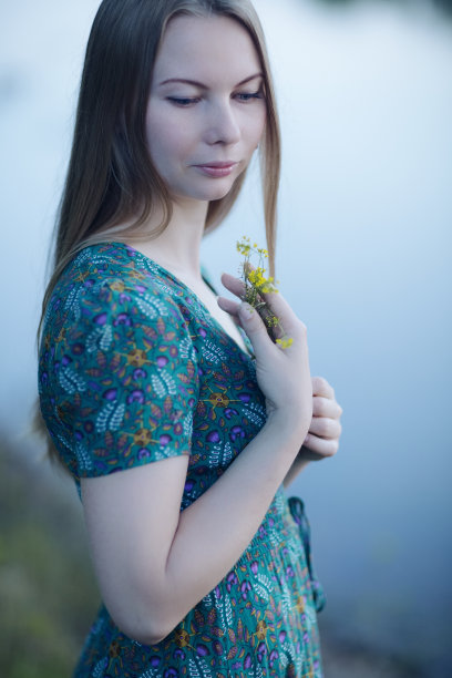 美丽的女孩穿着绿色的夏装，带着黄色的野花走在日落的湖边图片下载