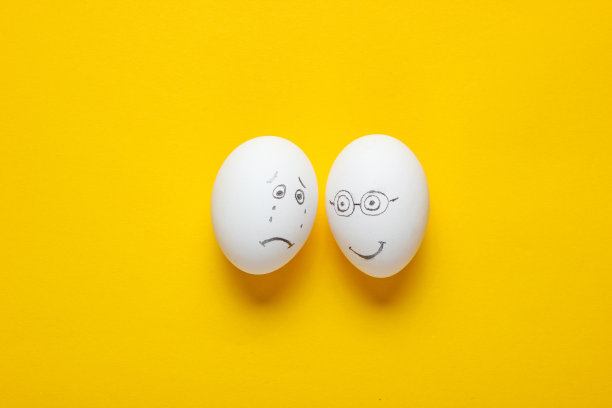 鸡蛋在黄色的背景上，悲伤和快乐的脸。俯视图图片下载
