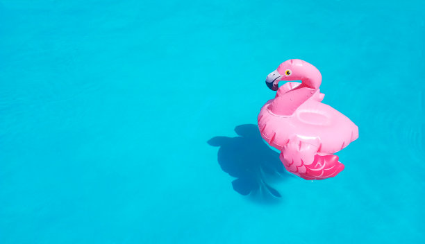 充气的粉红色火烈鸟在清澈湛蓝的池水中游泳。有一个地方是文本，复制空间。漂亮的海报，横幅或传单玩具。夏季新鲜的销售理念。图片下载