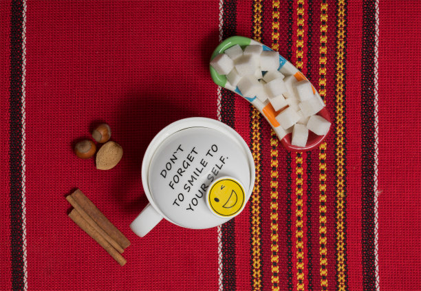 红色装饰桌布背景上的白色茶杯、肉桂棒和坚果图片下载