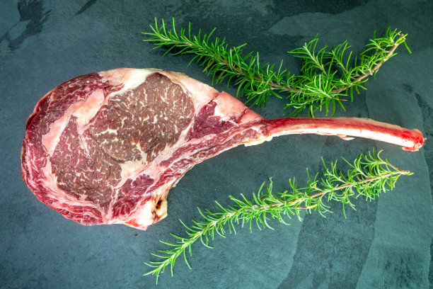 黑石餐桌上放着生的和牛战斧牛排和迷迭香。俯视图图片下载