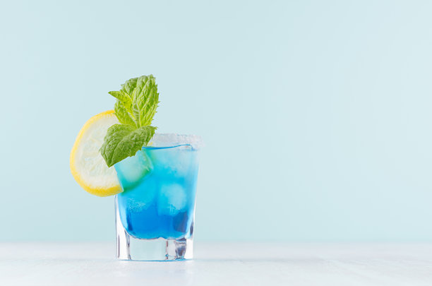 夏季冷蓝色泻湖饮料与冰块，盐边，绿色薄荷，柠檬片优雅的小酒杯在柔和的薄荷背景。图片下载