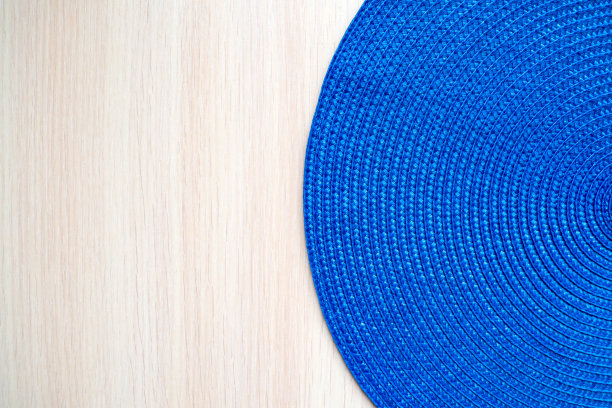 蓝色的圆形纺织垫子，米黄色的木制背景。图片下载