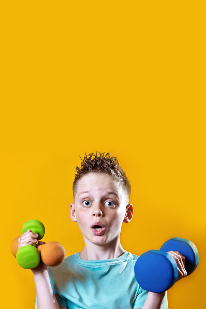 一个穿着亮t恤黄色背景上有哑铃的男孩图片下载